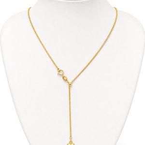 May include: A gold-tone necklace featuring a delicate chain with a sliding bead mechanism that allows for adjustable length. The chain terminates in a small, smooth, polished gold-tone heart charm suspended from the center of the Y-shaped design.
