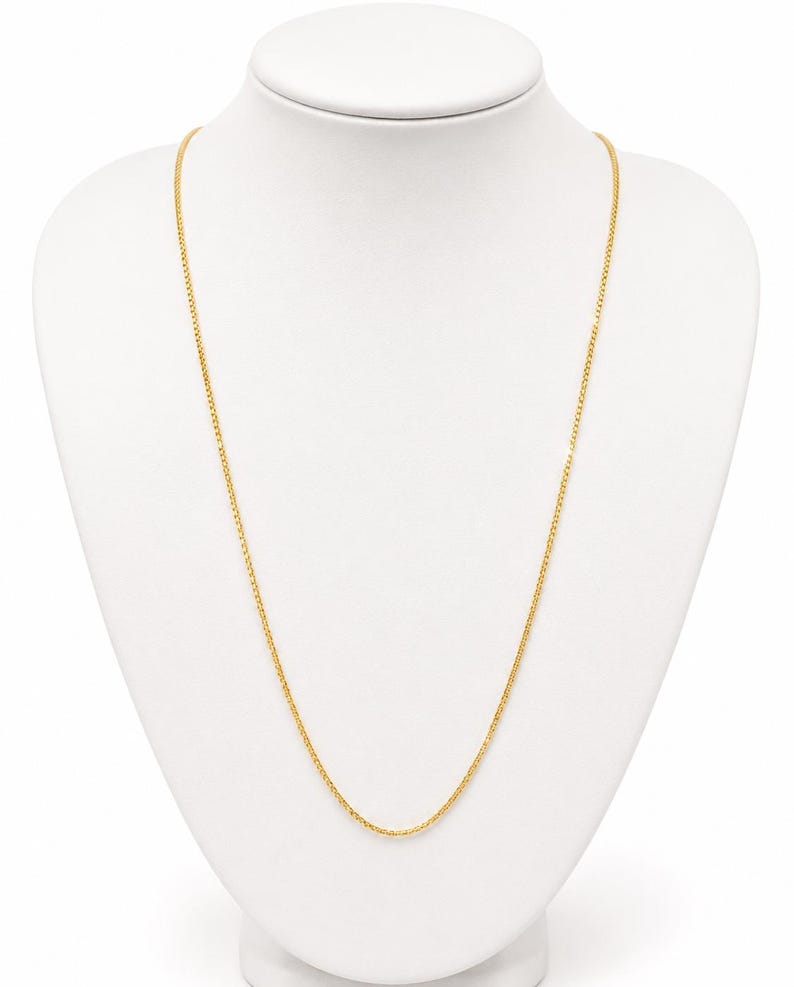 May include: A thin, yellow gold chain necklace featuring a delicate, interlocking wheat or spiga link design. The chain is uniform in color and texture, displaying a bright, polished metallic finish that hangs in a simple, smooth, and continuous loop.