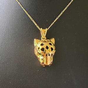 May include: A gold chain necklace with a detailed gold pendant shaped like a jaguar's head with green eyes.