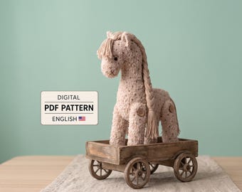 May include: A beige knitted horse toy with a long braided mane and tail, featuring small brown buttons at the joints, standing inside a small wooden four-wheeled cart. A rectangular sign displays the text DIGITAL PDF PATTERN ENGLISH.