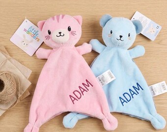 May include: Two soft plush security blankets, one pink cat and one blue bear, each featuring the name ADAM embroidered in matching thread. The cat has dark pink stripes on its head, and both toys include attached white product tags.