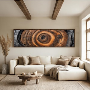 May include: A large, rectangular wooden wall art piece featuring a detailed cross-section of a tree trunk. The artwork showcases concentric rings in shades of brown, orange, and black, framed in dark wood. The piece hangs above a cream-colored sectional sofa.