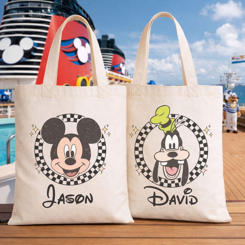May include: Two cream canvas tote bags with black handles. One bag features Mickey Mouse, the other Goofy, both within a chequered circle. The name "Jason" is printed under Mickey, and "David" under Goofy.
