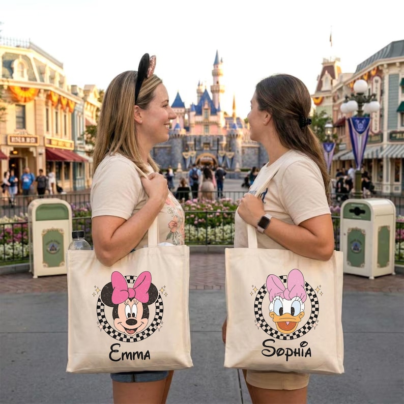 May include: Two cream-coloured canvas tote bags featuring Disney character designs. One shows Minnie Mouse with a pink bow, the other Daisy Duck with a pink bow. Both bags have a black and white checkered border and names below.