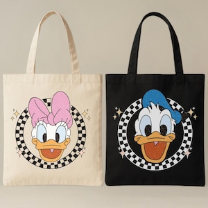 May include: Two tote bags with cartoon character designs. One is cream-coloured with Daisy Duck wearing a pink bow, inside a chequered circle. The other is black with Donald Duck wearing a blue hat, also in a chequered circle.