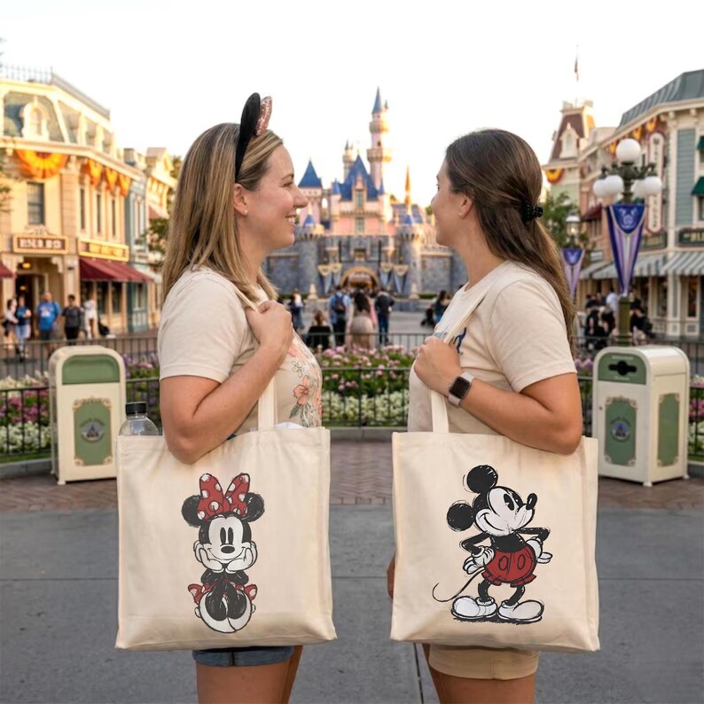 Puede incluir: Dos bolsas de lona, una con Minnie Mouse con lazo y vestido de lunares rojos, la otra Mickey Mouse con pantalones cortos rojos. Las bolsas son sostenidas por dos personas frente a un castillo.