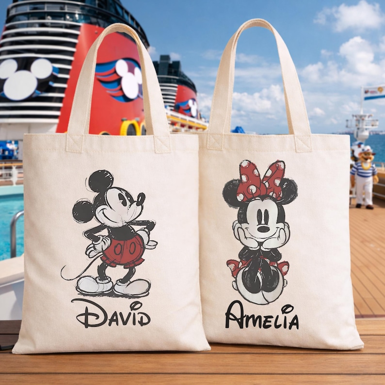Puede incluir: Dos bolsas de mano de lona color crema. Una bolsa presenta un boceto de Mickey Mouse con pantalones cortos rojos, con el nombre "David" debajo. La otra bolsa tiene un boceto de Minnie Mouse con un lazo de lunares rojos, con el nombre "Amelia" debajo.