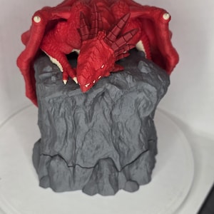 May include: A red dragon figurine with outstretched wings rests atop a gray, rocky base. The dragon has detailed scales and horns, with white accents on its wings and claws. This fantasy-themed collectible is a detailed sculpture.