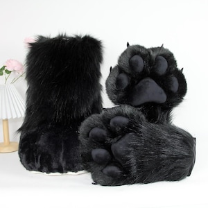 May include: Black furry paw-shaped costume feet and leg coverings. The paws have large, rounded pads and claws. The leg coverings are tall and cylindrical. The items are designed to resemble animal paws.