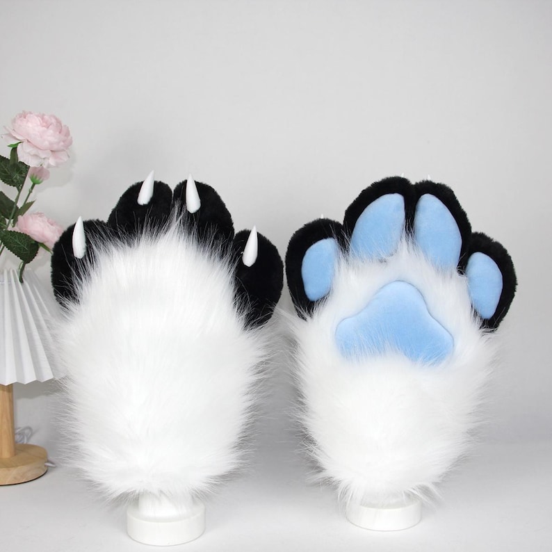 May include: A pair of furry paw gloves, one showing the top with black pads and white claws, the other showing the bottom with blue pads. The gloves are white with black accents.