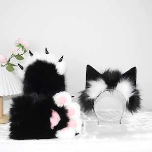 May include: A black and white cat paw glove set and a cat ear headband. The gloves have black claws and pink paw pads. The headband features black cat ears with white fur accents.