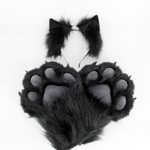 May include: A black furry costume set featuring a pair of paw-shaped gloves and a headband with cat ears. The gloves have gray paw pads and claws. The ears and gloves are made of soft, plush material.