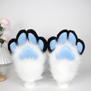 May include: A pair of furry paw gloves with a white base, black accents, and light blue paw pads. The gloves are designed to resemble animal paws, with a fluffy texture and a playful aesthetic.