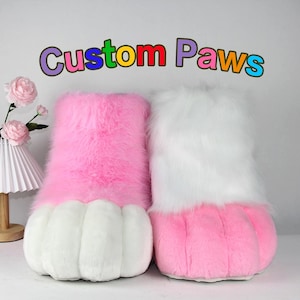 Könnte beinhalten: Paar plüschige, pelzige Pfoten-Hausschuhe. Ein Hausschuh ist rosa mit weißen Krallen, der andere ist weiß mit rosa Krallen. Der Text "Custom Paws" steht darüber.