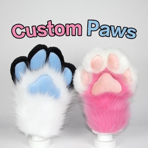 May include: Two custom-made furry paw gloves. One paw is white with black and light blue accents, the other is white with pink accents. The text "Custom Paws" is above the paws in pink and blue.