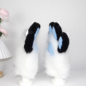 May include: A pair of furry paw gloves, featuring black and blue claws with white tips. The gloves have a fluffy white base. These cosplay accessories are designed to resemble animal paws.