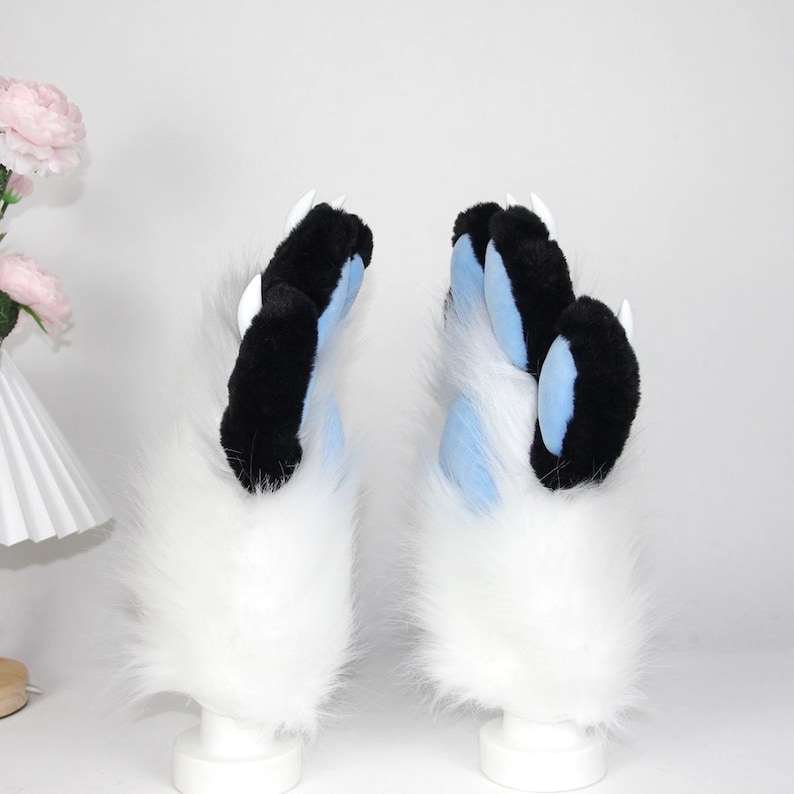 May include: A pair of furry paw gloves, featuring black and blue claws with white tips. The gloves have a fluffy white base. These cosplay accessories are designed to resemble animal paws.