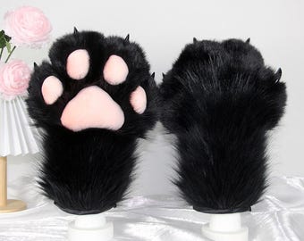 Può includere: Un paio di guanti neri a forma di zampa in finta pelliccia, con cuscinetti rosa e artigli neri. I guanti sono esposti su supporti bianchi su sfondo bianco. I guanti sono progettati per assomigliare a zampe di animali.