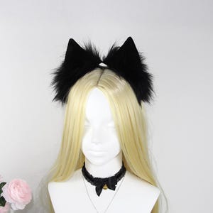 May include: A black faux fur cat ear headband with a matching black choker necklace featuring a small bow and a gold-colored bell. The mannequin has long, straight, blonde hair.