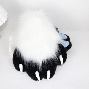 May include: A plush paw with black pads, white claws, and a large tuft of white fur. The paw has light blue accents and is designed to resemble an animal's paw. The item is likely a costume accessory or a novelty item.