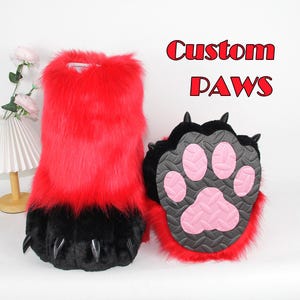 May include: A pair of plush animal-style gloves featuring vibrant red faux fur on the upper section and black faux fur on the lower section. The palms are black with textured pink paw pads and black claws. The text Custom PAWS is visible.