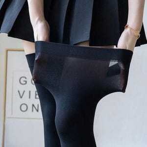 May include: Black opaque thigh-high stockings being held up, revealing the sheer fabric. The stockings are paired with a black pleated skirt. The image is set against a neutral background.