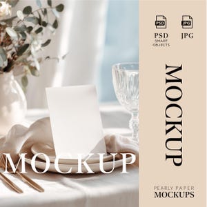 May include: A mockup scene featuring a blank white card on a plate with gold cutlery, a crystal wine glass, and a vase with greenery. The word "MOCKUP" is displayed on the card and on the beige background. The words "PSD SMART OBJECTS" and "JPG" are also visible.