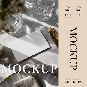 May include: A white blank card sits on a white tablecloth, next to a gold-colored knife and a decorative plate. The image includes crystal glassware and the word "MOCKUP" in large, elegant font. The image also includes the text "PSD SMART OBJECTS" and "JPG".
