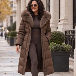 May include: A long brown puffer coat featuring a large, plush faux fur collar, long sleeves, and a quilted design. The coat is worn over a matching brown long-sleeved top and leggings, paired with brown ankle boots and brown-tinted sunglasses.