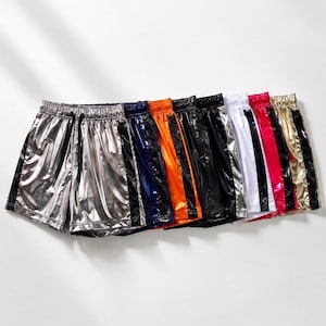 May include: A collection of shiny athletic shorts in various colors, including silver, black, navy, orange, and gold. Each pair features a contrasting stripe down the side and an elastic waistband with a drawstring.