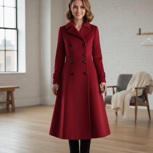 Puede incluir: Un abrigo largo rojo de doble botonadura con botones negros. El abrigo tiene un corte entallado y una falda acampanada. La modelo lleva pantalones negros. El abrigo es de estilo clásico.
