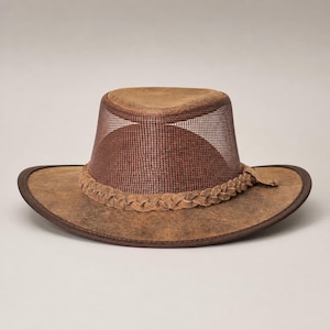May include: A brown hat with a wide brim and a mesh crown. The hat features a braided band around the base of the crown and a solid brown top panel. The brim has a dark brown edge trim, and the overall texture of the material appears weathered.