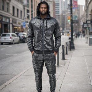 May include: A black and grey tracksuit featuring a geometric pattern. The hooded jacket has a zip closure, and the trousers have a matching design. The outfit is worn by a person standing on a city pavement.