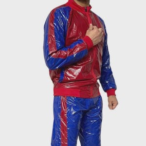 Può includere: Una tuta rossa e blu. La giacca è rossa con strisce blu sulle maniche e colletto e polsini rossi. I pantaloni sono blu con strisce rosse sui lati. La tuta ha un aspetto lucido, simile alla plastica.