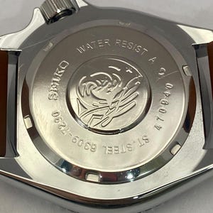 K&ouml;nnte beinhalten: Nahaufnahme des Geh&auml;usebodens einer Edelstahl-Uhr mit braunem Lederarmband. Das Zifferblatt der Uhr tr&auml;gt die Aufschrift "WATER RESIST A", "SEIKO", "ST. STEEL" und "6309-7290". Die Uhr hat auch die Nummer "470940".