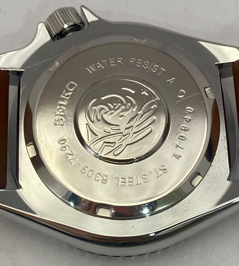 K&ouml;nnte beinhalten: Nahaufnahme des Geh&auml;usebodens einer Edelstahl-Uhr mit braunem Lederarmband. Das Zifferblatt der Uhr tr&auml;gt die Aufschrift "WATER RESIST A", "SEIKO", "ST. STEEL" und "6309-7290". Die Uhr hat auch die Nummer "470940".