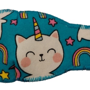 May include: A turquoise eye patch with a white unicorn cat design. The cat has a pink nose and yellow stars are scattered across the patch.