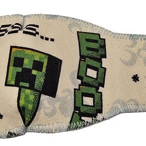 May include: A Minecraft-themed eye patch with a green Creeper face and the word "BOOM" in green block letters. The patch has a black elastic cord and a small TNT graphic.