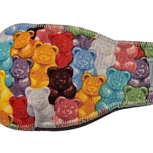 May include: A colorful eye patch with a gummy bear pattern. The patch is made of fabric and has a gray elastic strap.