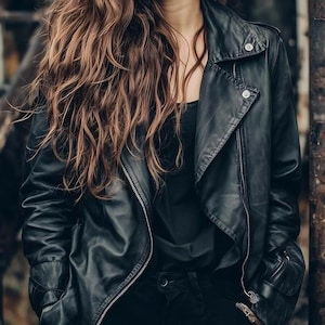 Könnte beinhalten: Schwarze Lederjacke im klassischen Biker-Stil mit Reverskragen, asymmetrischem Reißverschluss und Druckknopfdetails. Die Jacke wird über einem schwarzen Oberteil und mit einer schwarzen Hose getragen. Das Model hat lange, wellige, braune Haare.