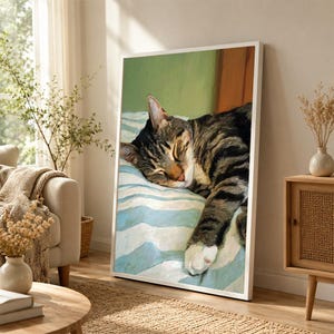 May include: A framed wall art print featuring an oil painting style depiction of a brown and black tabby cat sleeping on a light blue and white striped surface. The cat has closed eyes and a white paw resting on the fabric against a green wall.