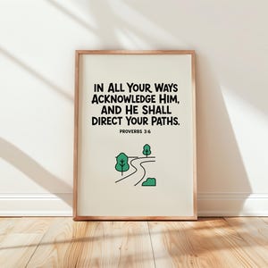 Op de afbeelding: Een ingelijste wandkunstprint met een lichtcrème achtergrond en zwarte tekst: IN ALL YOUR WAYS ACKNOWLEDGE HIM, AND HE SHALL DIRECT YOUR PATHS. PROVERBS 3:6. Onder de tekst staat een groene lijntekening van een kronkelende weg en bomen.