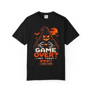 Op de afbeelding: Een zwart t-shirt met korte mouwen en een afbeelding van een figuur met een pompoenhoofd in een capuchon die een gamecontroller vasthoudt. De tekst luidt GAME OVER? NOT TODAY met drie gepixelde hartjes en een PRESS START-knop in oranje en wit.