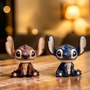 May include: Two small, stylized figurines of a cartoon character. One is brown with tan ears, the other is blue with tan ears. Both have large black eyes and are seated with their arms and legs tucked in.