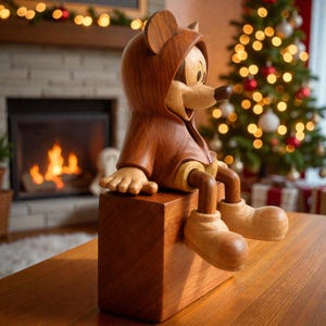 Pu&ograve; includere: Una statuetta di legno di un personaggio dei cartoni animati con un cappotto con cappuccio, seduto su un blocco di legno. La statuetta &egrave; marrone e beige, con un design dettagliato. Lo sfondo include un camino, un albero di Natale e luci decorative.