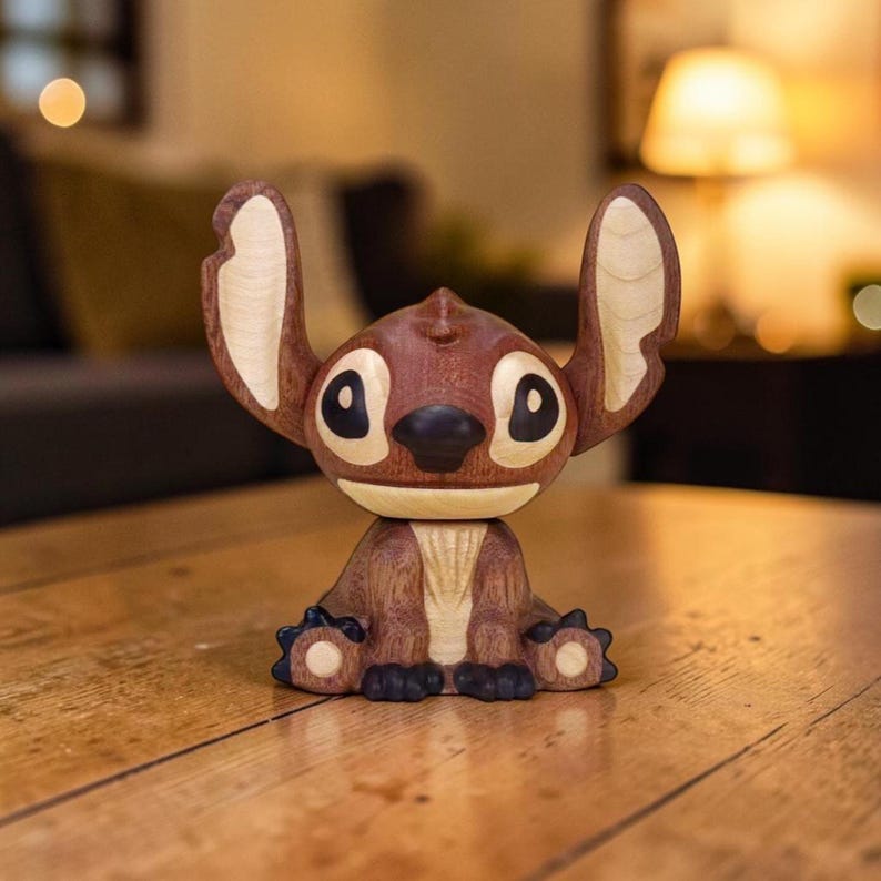 May include: A wooden figurine of Stitch, the Disney character, in a seated position. The figurine is primarily brown with lighter wood accents on the ears and chest. It has large black eyes and a dark blue nose and feet. The figurine is on a wooden surface.