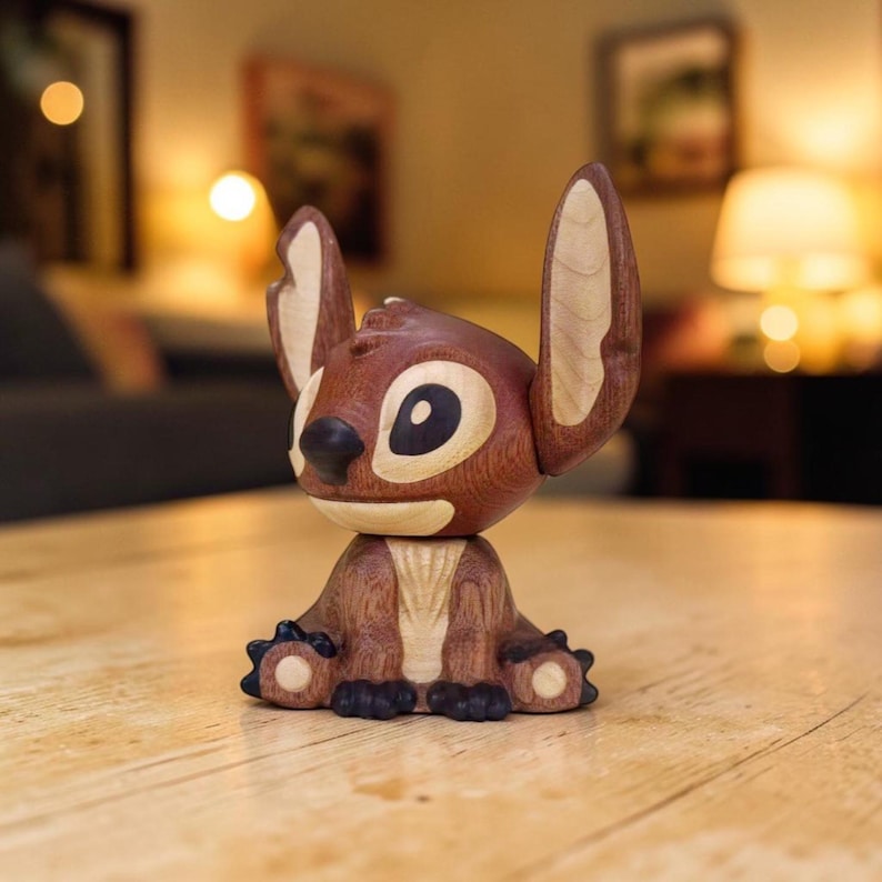 May include: A wooden figurine of the character Stitch from the animated film Lilo & Stitch. The figurine is primarily brown with lighter wood accents on the ears and face. It is sitting on a wooden surface.