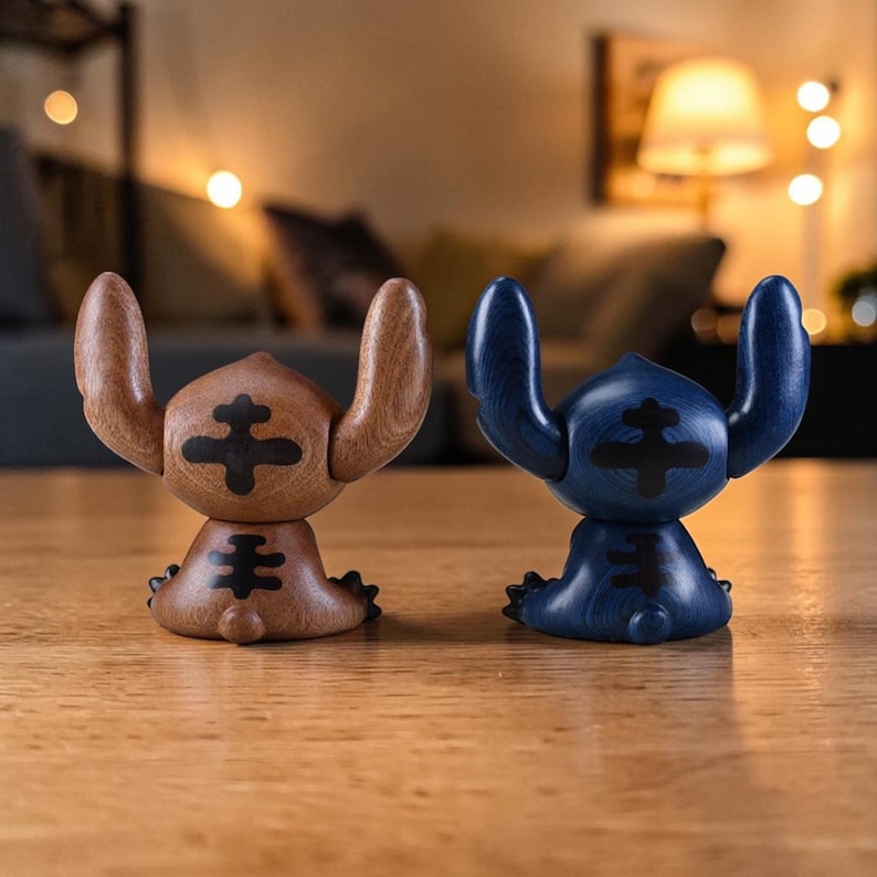May include: Two wooden figurines of a cartoon character, one brown and one blue, are displayed on a wooden surface. The figurines have large ears and a distinctive cross-shaped design on their bodies. The background is softly blurred with warm lighting.