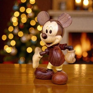 May include: A wooden Mickey Mouse figurine with a light brown face and ears, a dark brown body, and light-colored gloves and shoes. The figure is posed on a wooden surface, with a blurred Christmas tree and fireplace in the background.