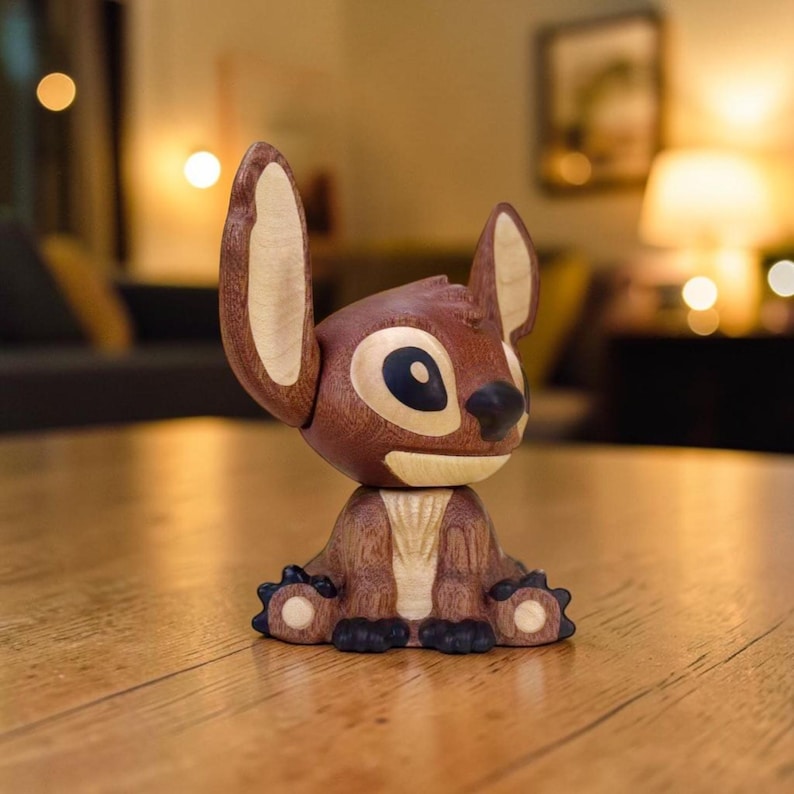 May include: A wooden figurine of the character Stitch from the Disney movie Lilo & Stitch. The figurine is brown with light-colored wood accents on the ears and belly. The eyes are black and blue. The figurine is sitting on a wooden surface.